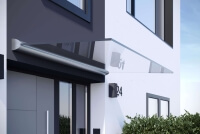 Vordach aus Glas in freitragender Optik an grauer Hausfassade mit ovalem Profil